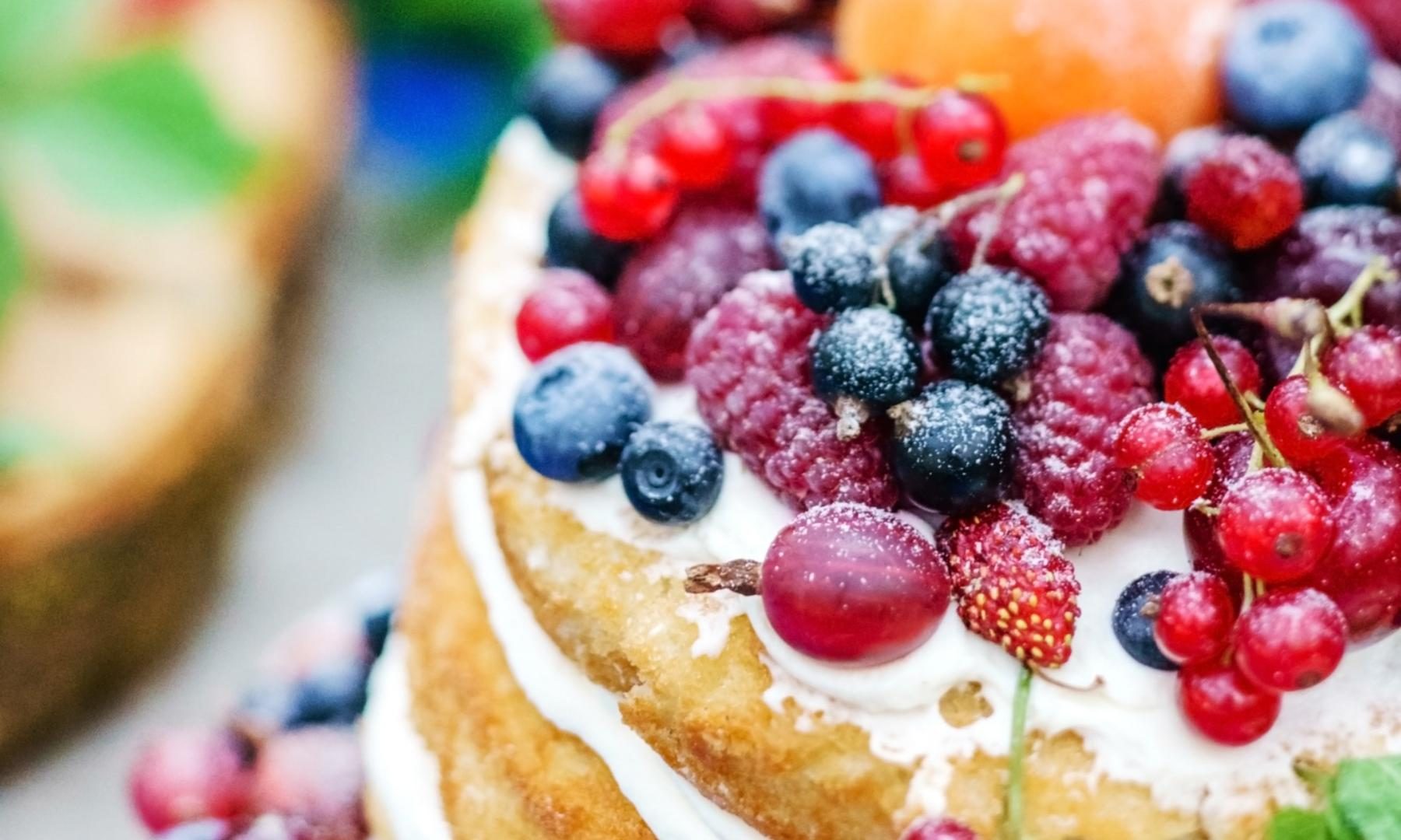 Wedding cake topped with fresh berries and cream, dusted with icing sugar for a summer celebration
