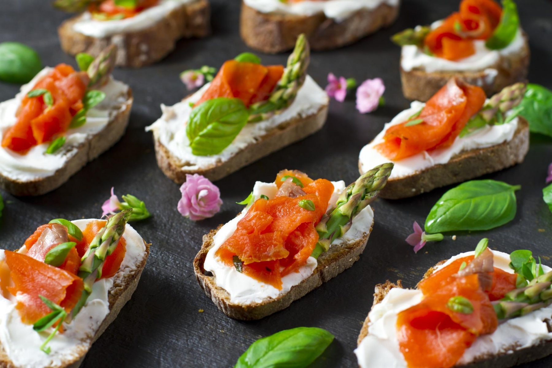 Smoked salmon and cream cheese crostini canapés garnished with asparagus and fresh herbs